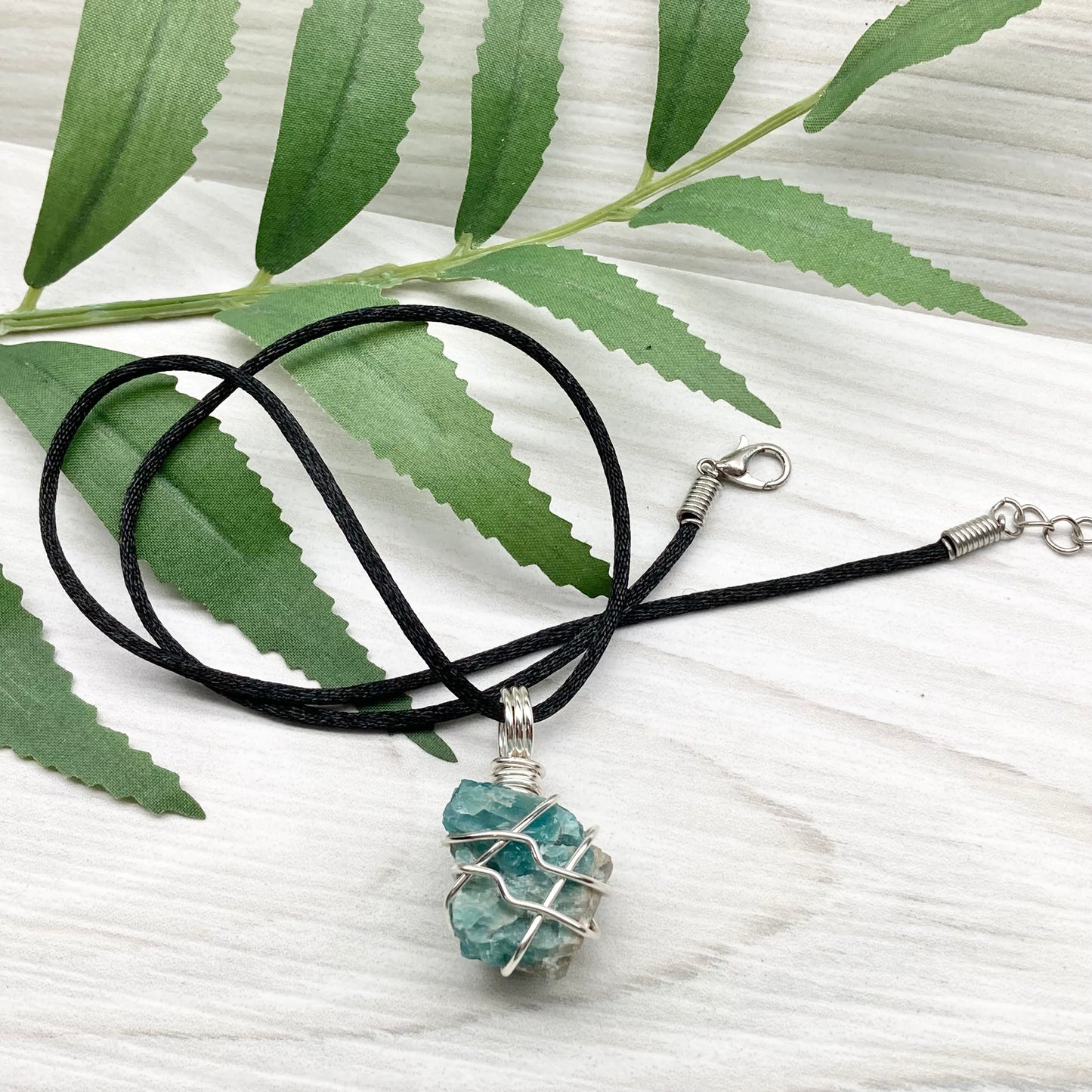Blue Apatite necklace. Blue stone wrapped with silver copper wire. Hangs on a black chain.