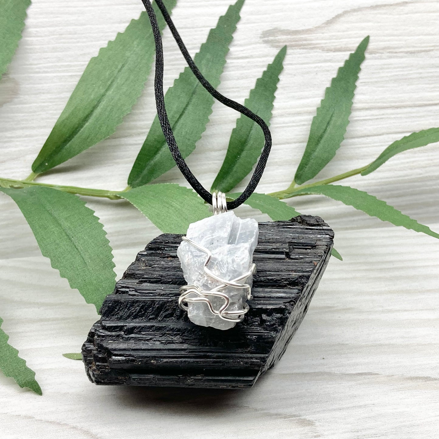 Natural Blue Calcite Necklace. Blue Calcite crystal wrapped with tarnish resistant silver colored copper wire. Pendant comes on a black lobster claw necklace with silver ends.