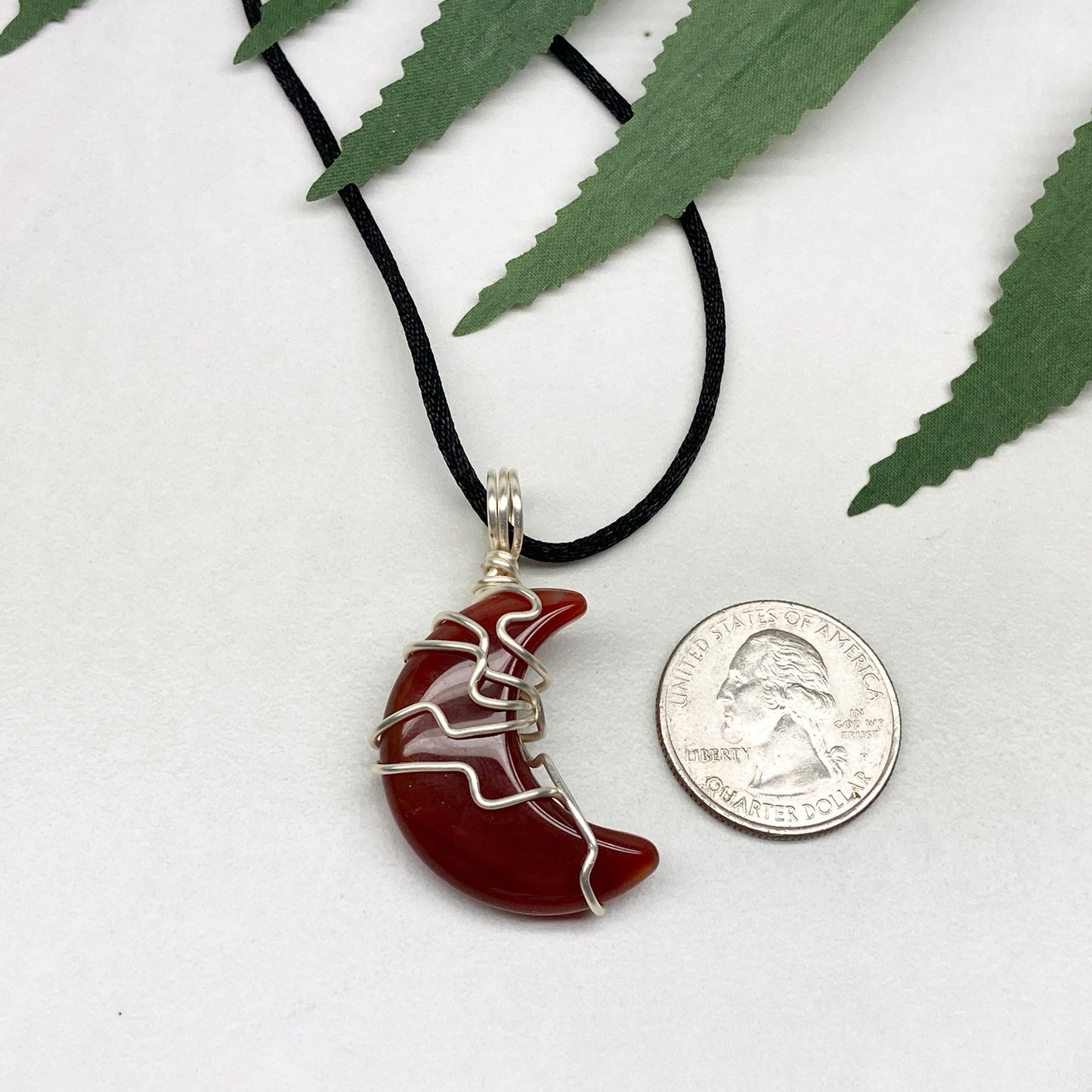 Carnelian crescent moon necklace wrapped in silver-colored copper wire on a black necklace. One-of-a-kind pendant handmade during the Moon in Cancer.