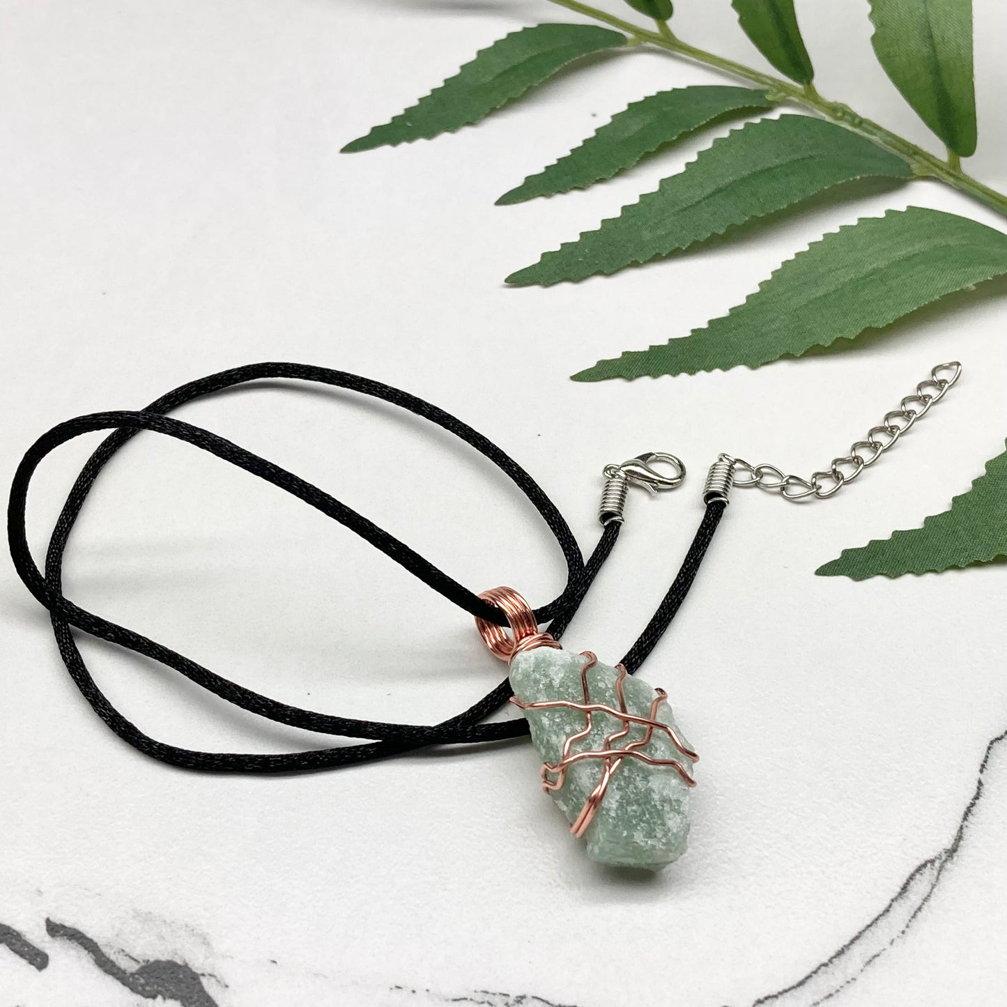 Necklace with a green stone pendant on a white surface with green leaves.