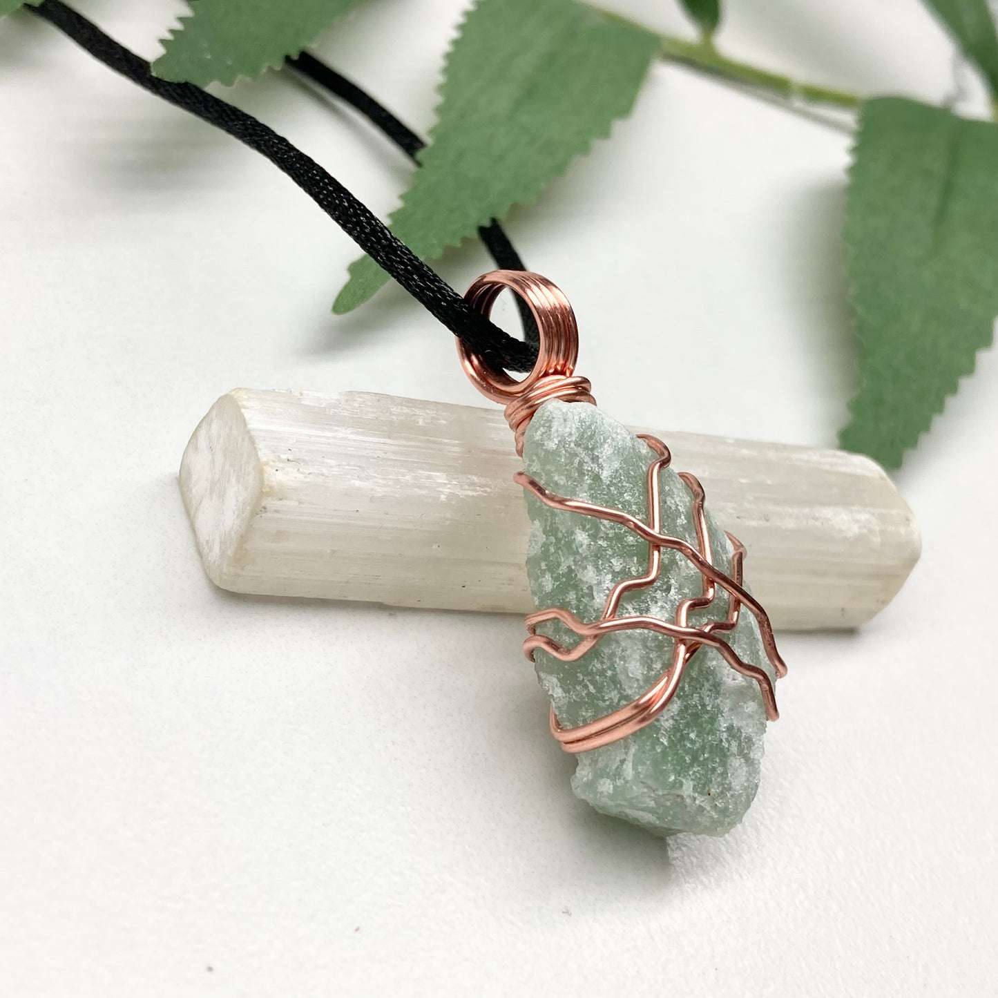 Green stone pendant with copper wire wrapping on a white background