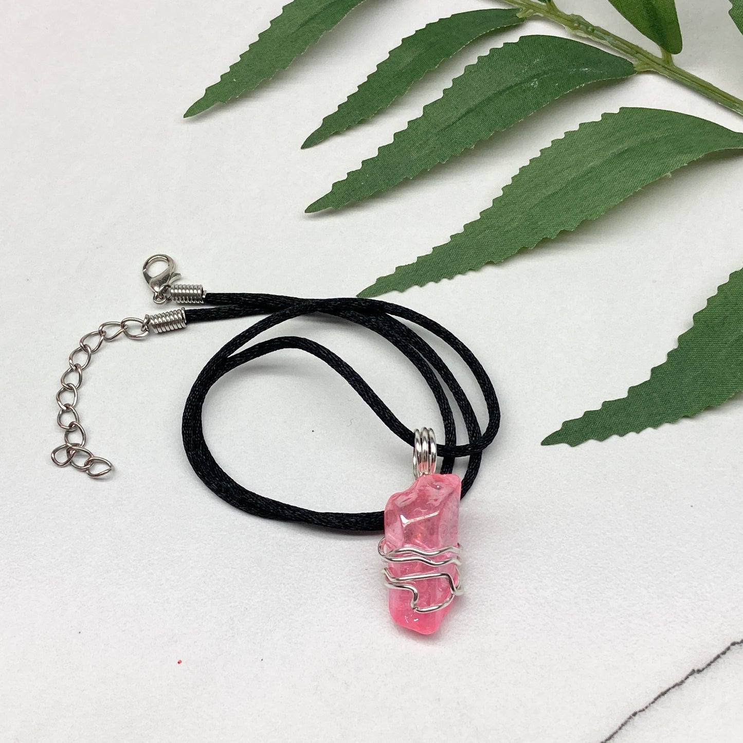Pink Aura Quartz necklace featuring a natural crystal point coated in pink aura for a glowing effect, hand-wrapped with silver wire, on a black chain for everyday wear.