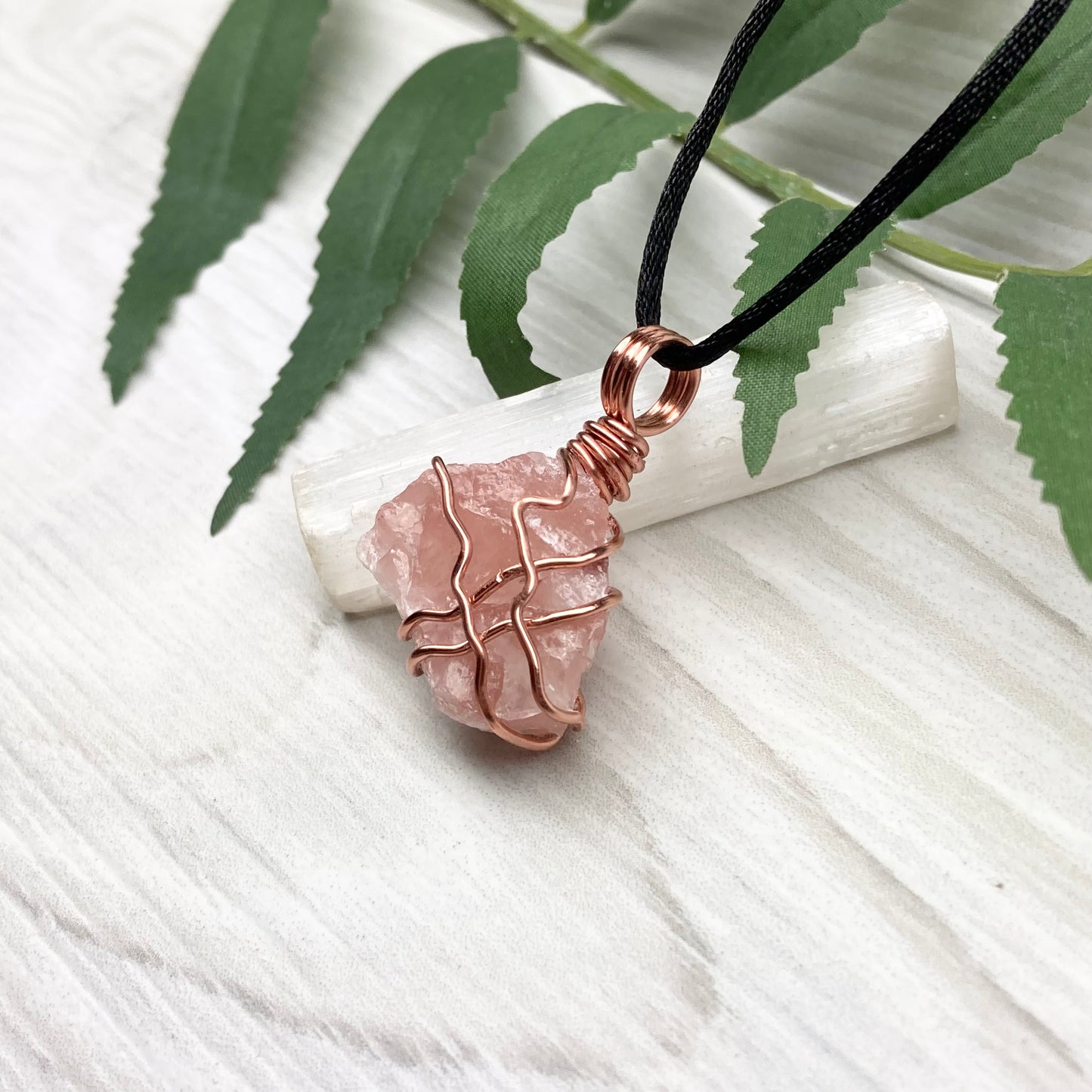 Necklace with a pink calcite stone pendant on a white background with green leaves.