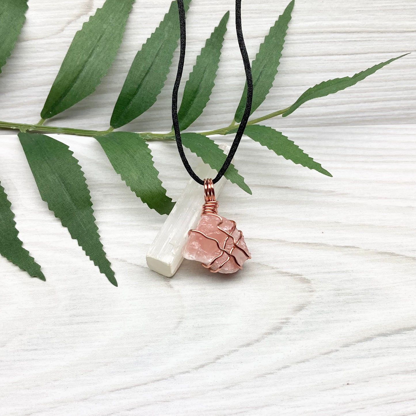 Necklace with a pink calcite stone pendant on a white background with green leaves.