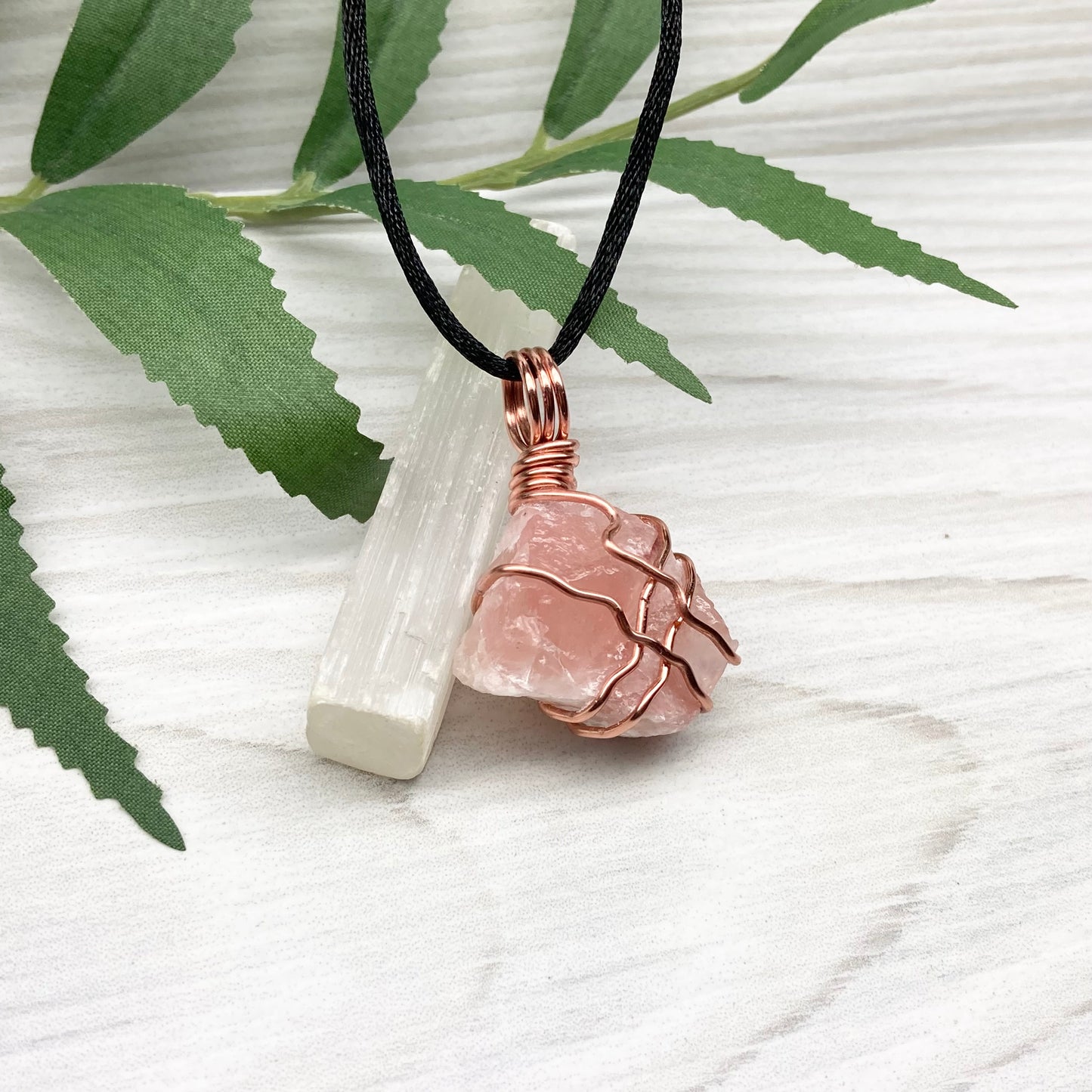 Necklace with a pink calcite stone pendant on a white background with green leaves.