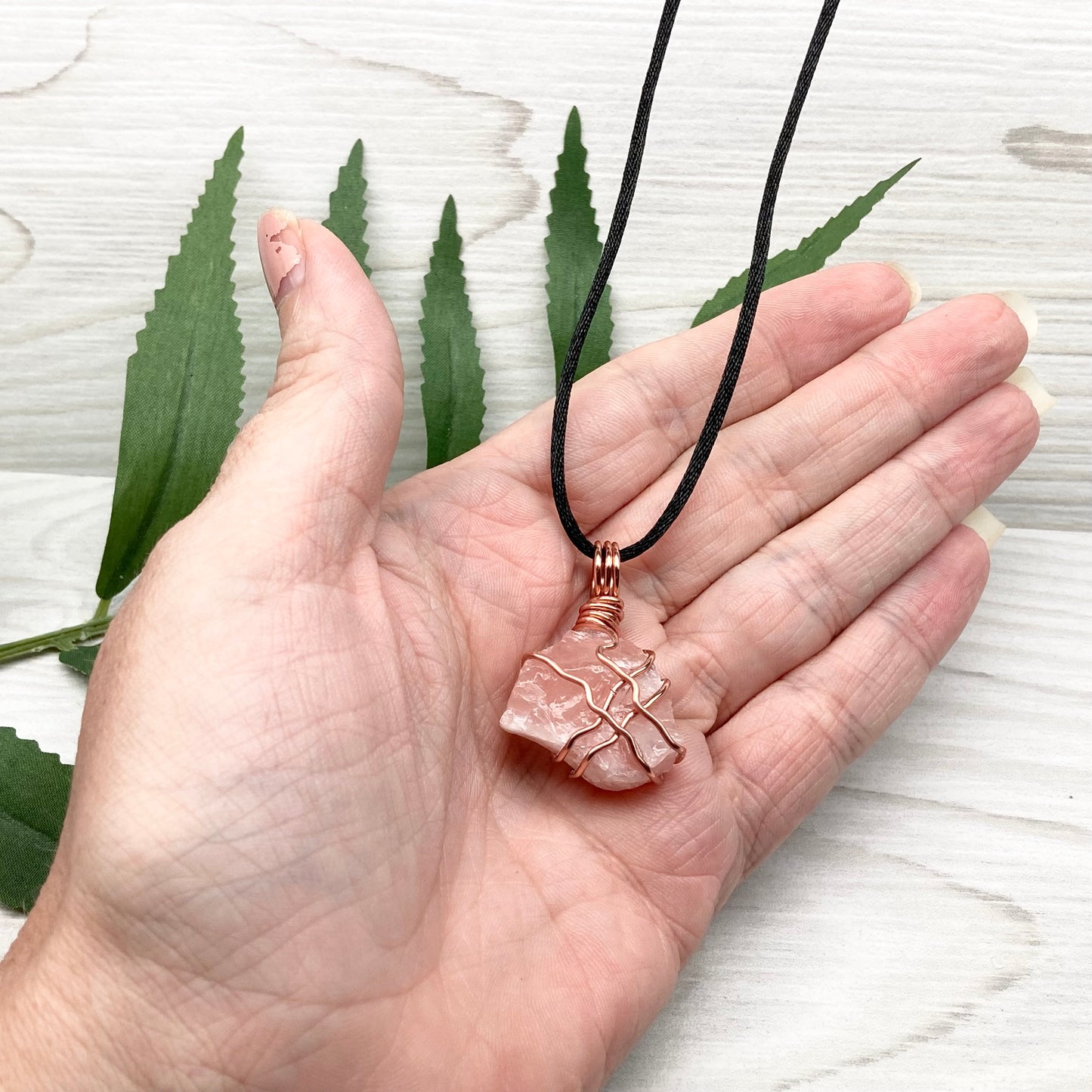 Necklace with a pink calcite stone pendant on a white background with green leaves.