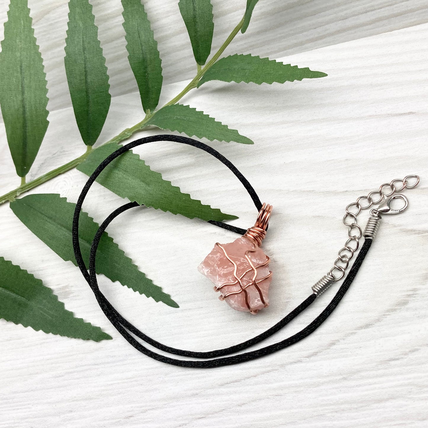 Necklace with a pink calcite stone pendant on a white background with green leaves.