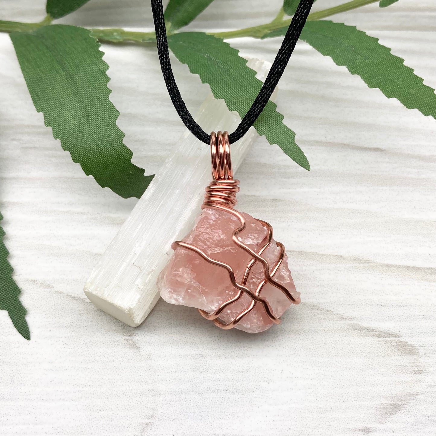 Necklace with a pink calcite stone pendant on a white background with green leaves.