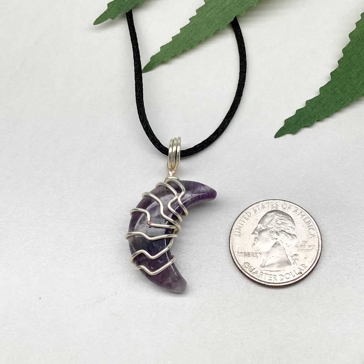 Purple Amethyst crescent moon necklace wrapped in silver-colored copper wire and hanging on a black chain. Handmade during the Moon in Leo.