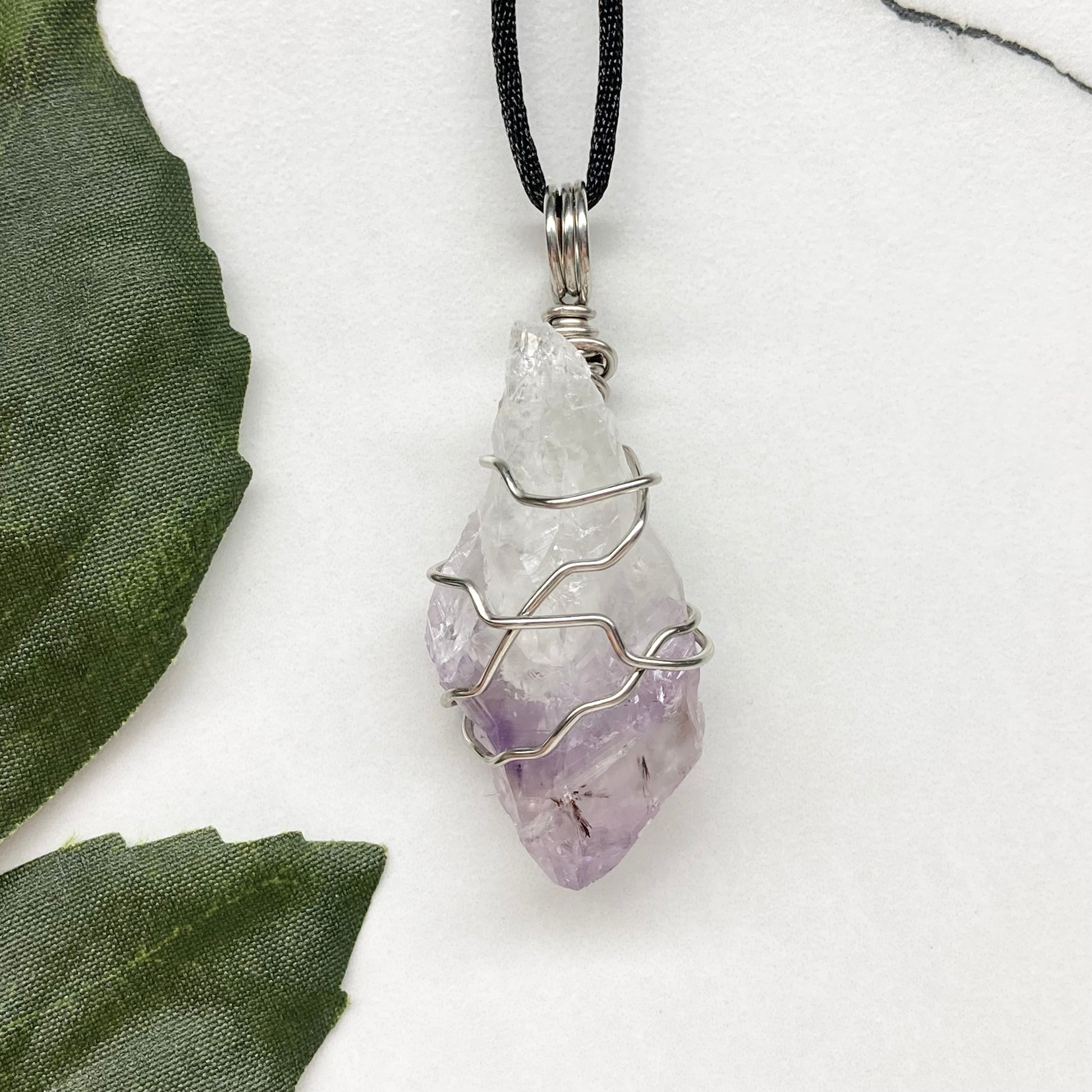 Amethyst tip necklace. Beautiful unique crystal that is Clear Quartz for the top half and purple amethyst for the bottom half. Crystal is wrapped with silver copper wire. Hangs on a black chain.