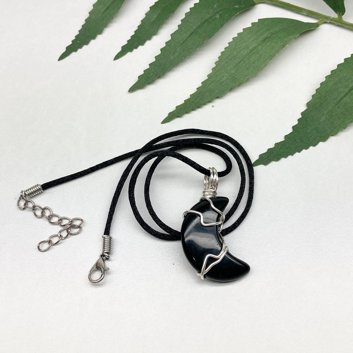 Black Onyx crescent moon necklace wrapped in silver-colored copper wire on a black necklace. One-of-a-kind pendant handmade during the Moon in Pisces.