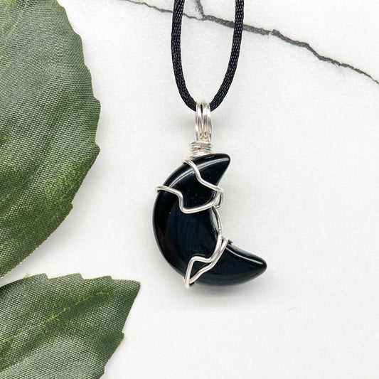 Black Onyx crescent moon necklace wrapped in silver-colored copper wire on a black necklace. One-of-a-kind pendant handmade during the Moon in Pisces.