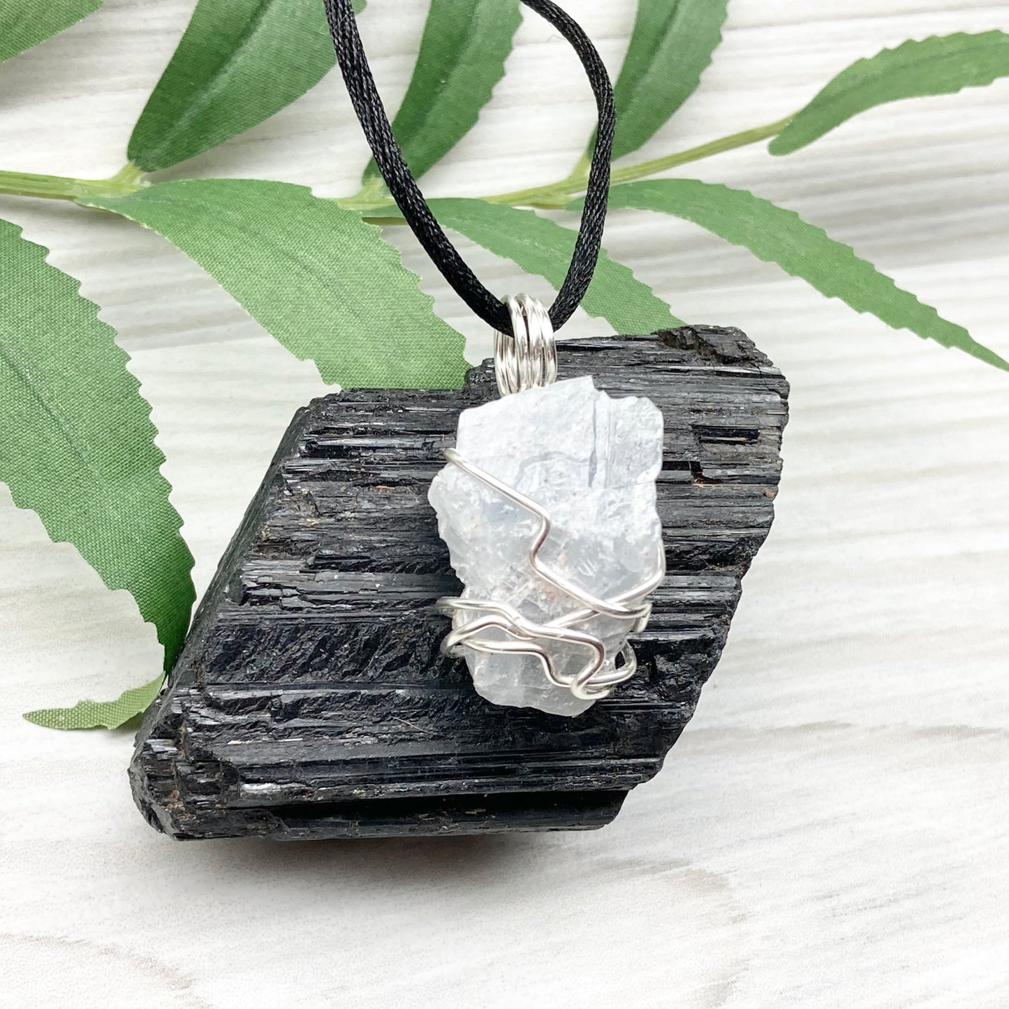 Natural Blue Calcite Necklace. Blue Calcite crystal wrapped with tarnish resistant silver colored copper wire. Pendant comes on a black lobster claw necklace with silver ends.