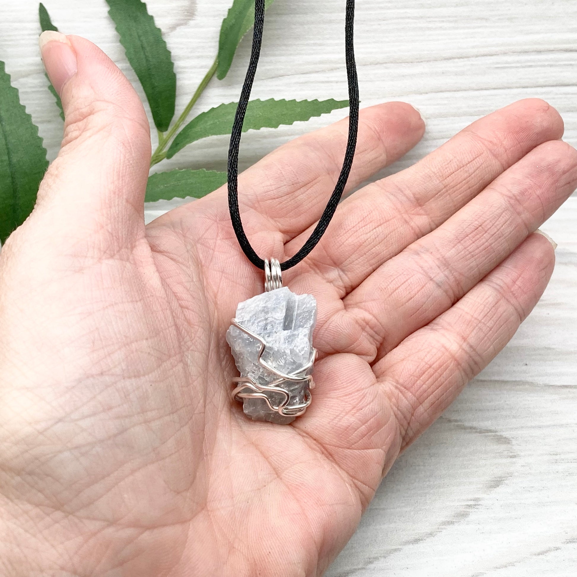 Natural Blue Calcite Necklace. Blue Calcite crystal wrapped with tarnish resistant silver colored copper wire. Pendant comes on a black lobster claw necklace with silver ends.