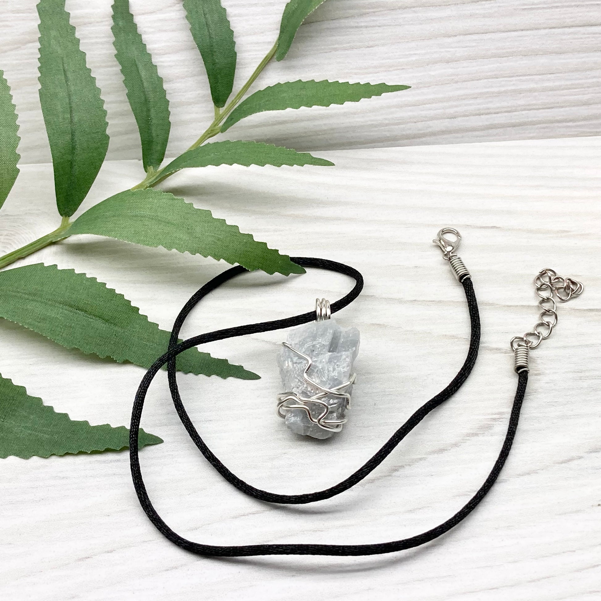 Natural Blue Calcite Necklace. Blue Calcite crystal wrapped with tarnish resistant silver colored copper wire. Pendant comes on a black lobster claw necklace with silver ends.