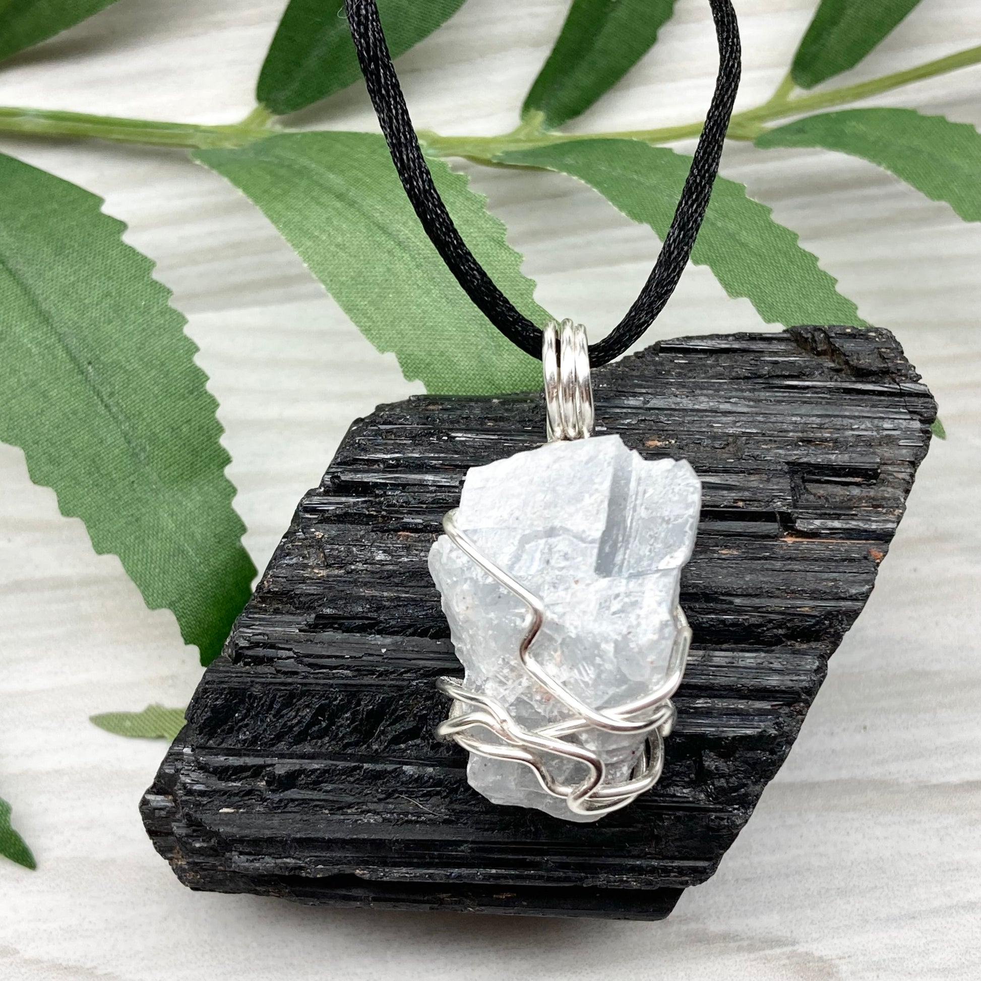 Natural Blue Calcite Necklace. Blue Calcite crystal wrapped with tarnish resistant silver colored copper wire. Pendant comes on a black lobster claw necklace with silver ends.