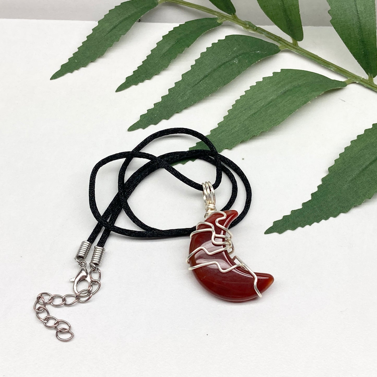 Carnelian crescent moon necklace wrapped in silver-colored copper wire on a black necklace. One-of-a-kind pendant handmade during the Moon in Cancer.
