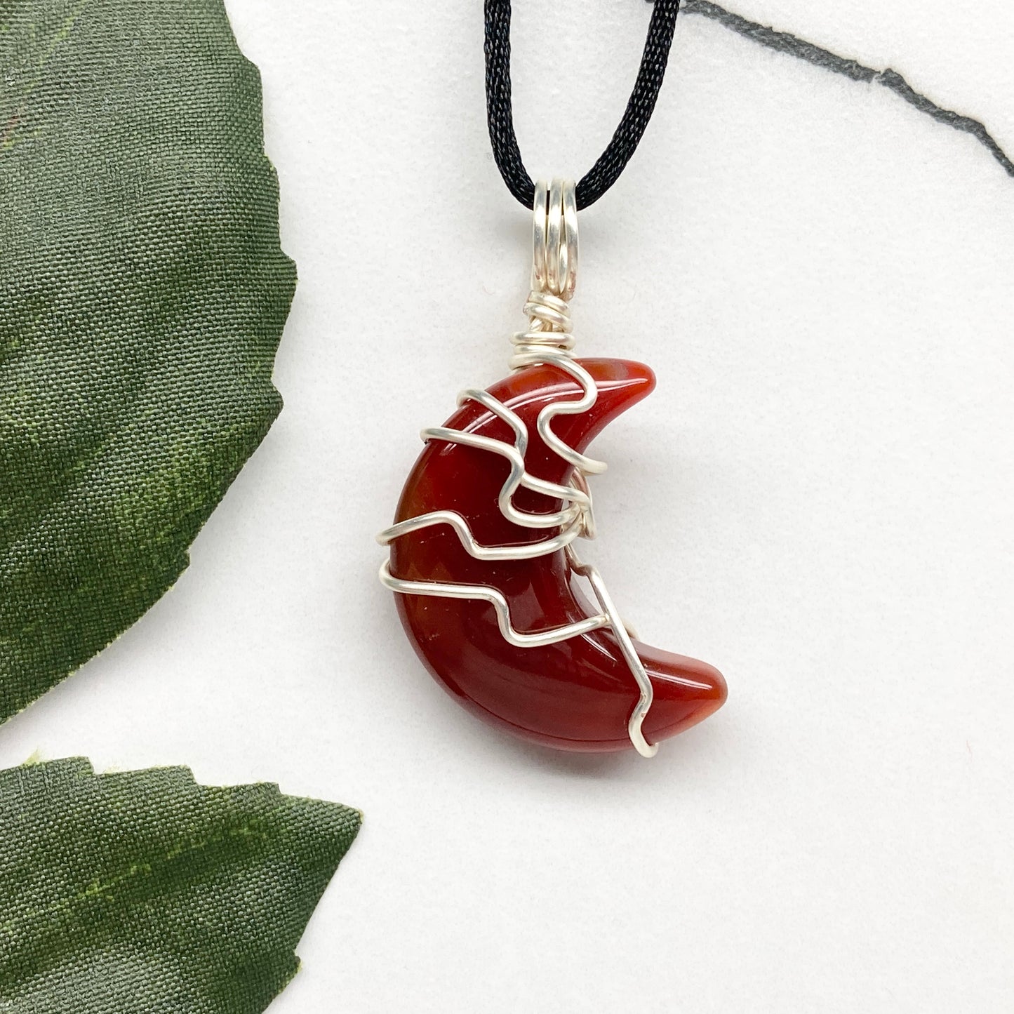Carnelian crescent moon necklace wrapped in silver-colored copper wire on a black necklace. One-of-a-kind pendant handmade during the Moon in Cancer.