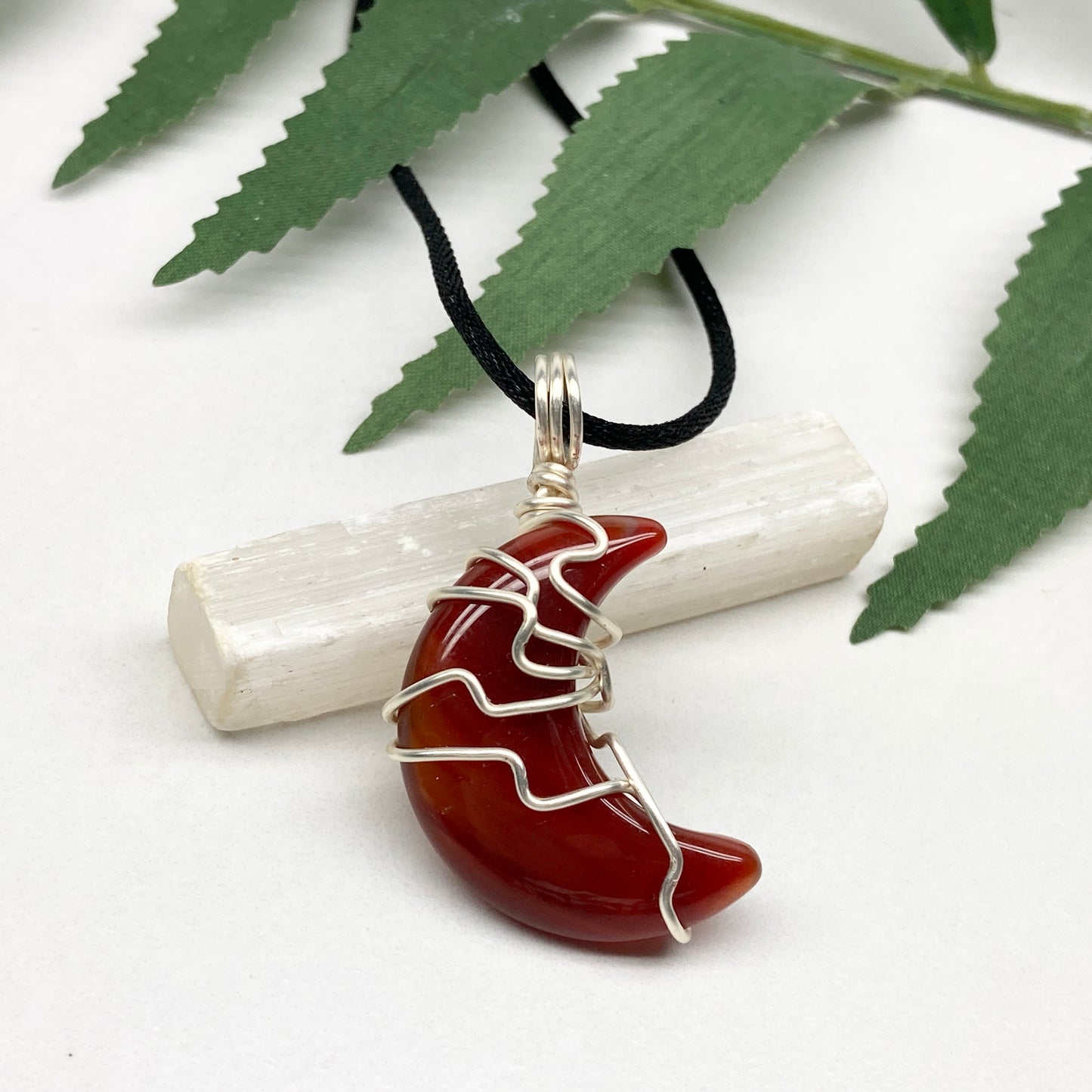 Carnelian crescent moon necklace wrapped in silver-colored copper wire on a black necklace. One-of-a-kind pendant handmade during the Moon in Cancer.