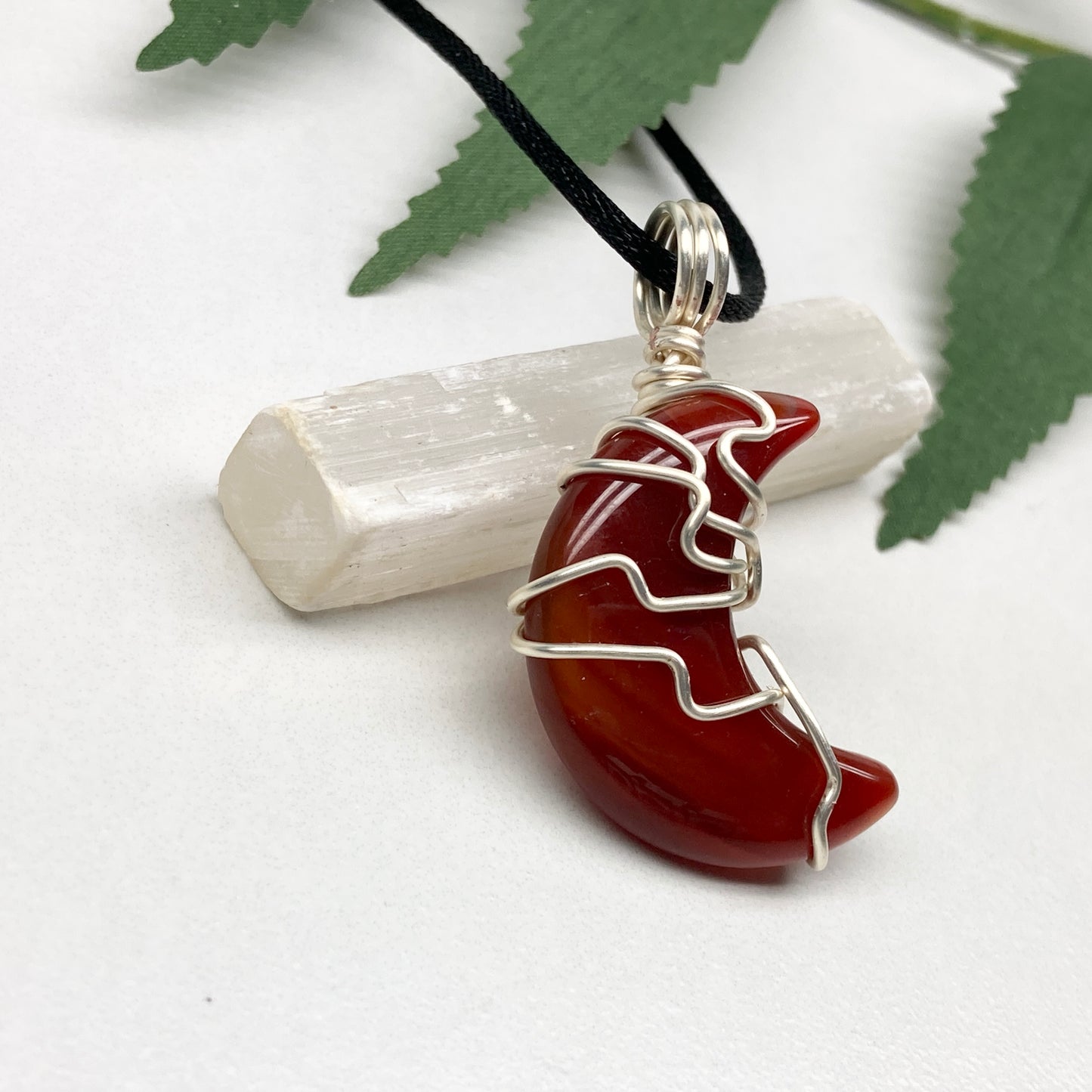 Carnelian crescent moon necklace wrapped in silver-colored copper wire on a black necklace. One-of-a-kind pendant handmade during the Moon in Cancer.