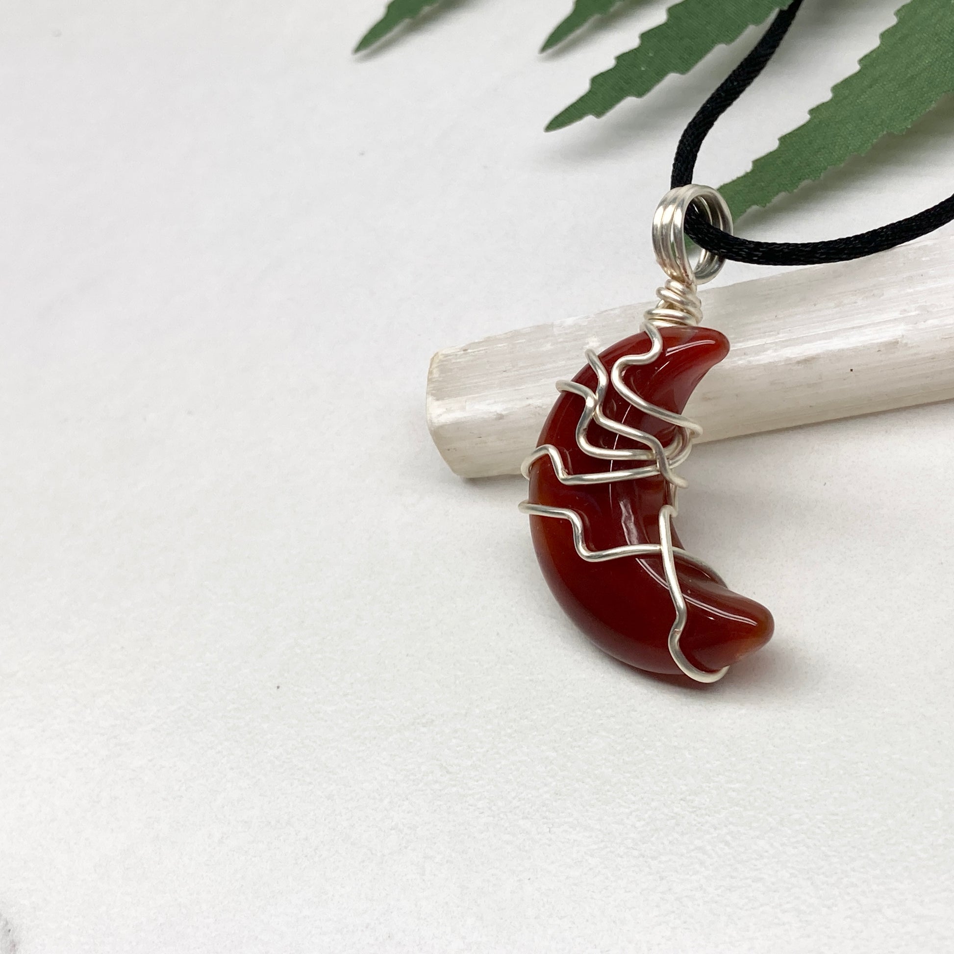 Carnelian crescent moon necklace wrapped in silver-colored copper wire on a black necklace. One-of-a-kind pendant handmade during the Moon in Cancer.