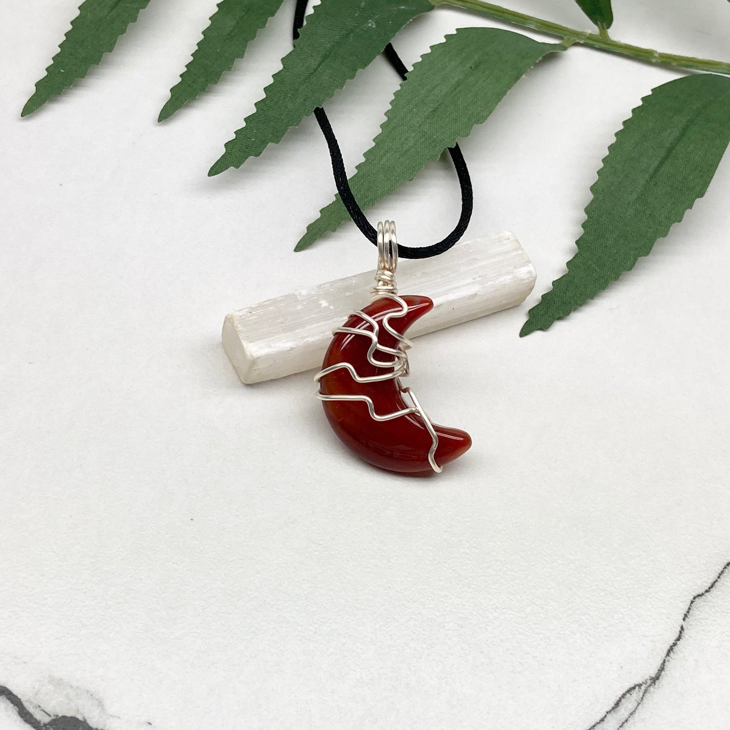 Carnelian crescent moon necklace wrapped in silver-colored copper wire on a black necklace. One-of-a-kind pendant handmade during the Moon in Cancer.