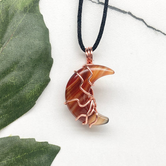 Carnelian Moon necklace. Moon shaped Carnelian crystal wrapped with copper wire. Hangs on a black chain. Celestial witchcore jewelry.
