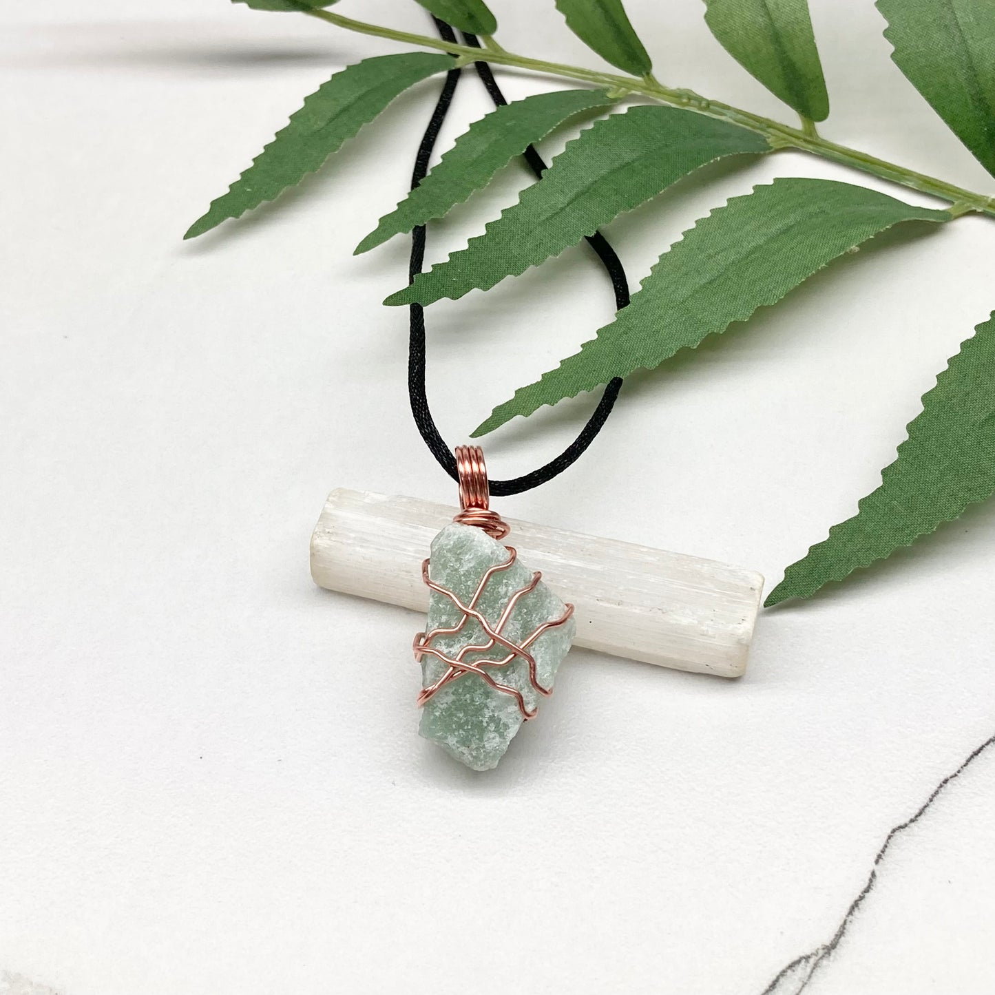Necklace with a green stone pendant on a white surface with leaves in the background