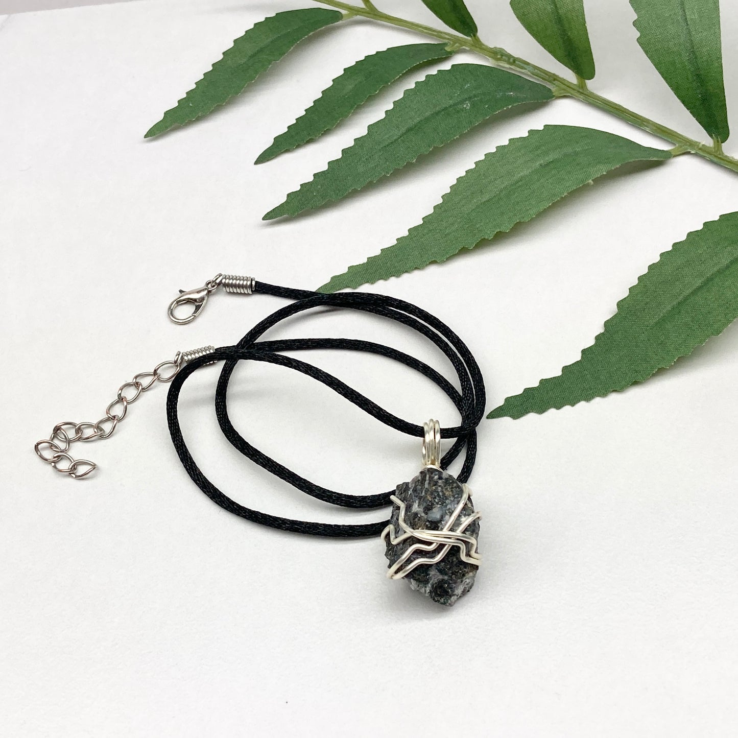 Indigo Gabbro necklace. Raw Indigo Gabbro stone wrapped with tarnish resistant wire. Hangs on a black chain. Also known as Mystic Merlinite. Gray and black marbled crystal.