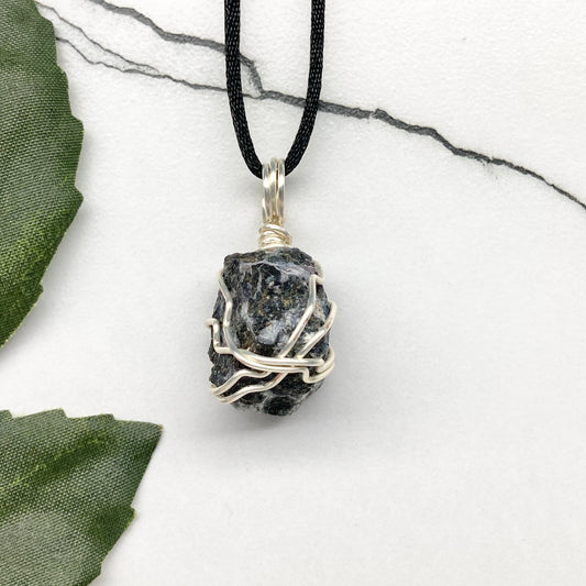 Indigo Gabbro necklace. Raw Indigo Gabbro stone wrapped with tarnish resistant wire. Hangs on a black chain. Also known as Mystic Merlinite. Gray and black marbled crystal.