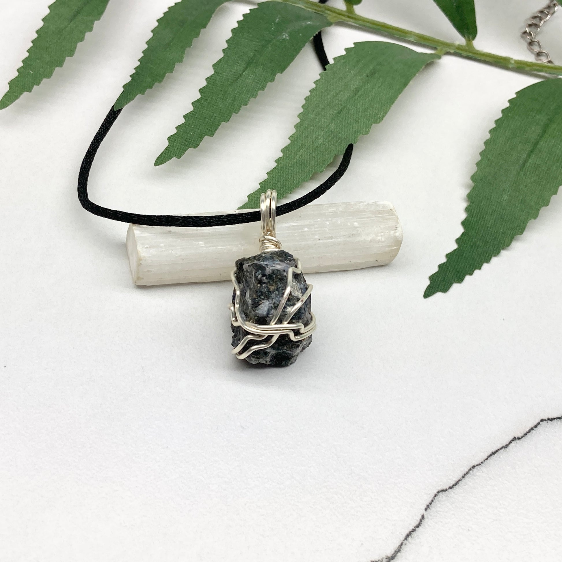 Indigo Gabbro necklace. Raw Indigo Gabbro stone wrapped with tarnish resistant wire. Hangs on a black chain. Also known as Mystic Merlinite. Gray and black marbled crystal.