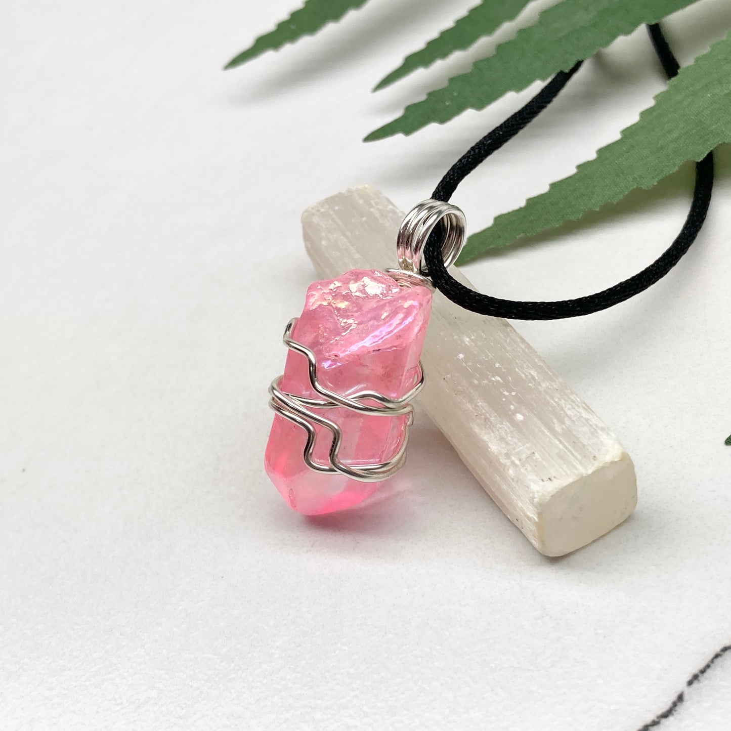 Pink Aura Quartz necklace. Pink Aura Quartz crystal wrapped with silver colored copper wire. Hangs on a black chain. Wire wrapped pendant.