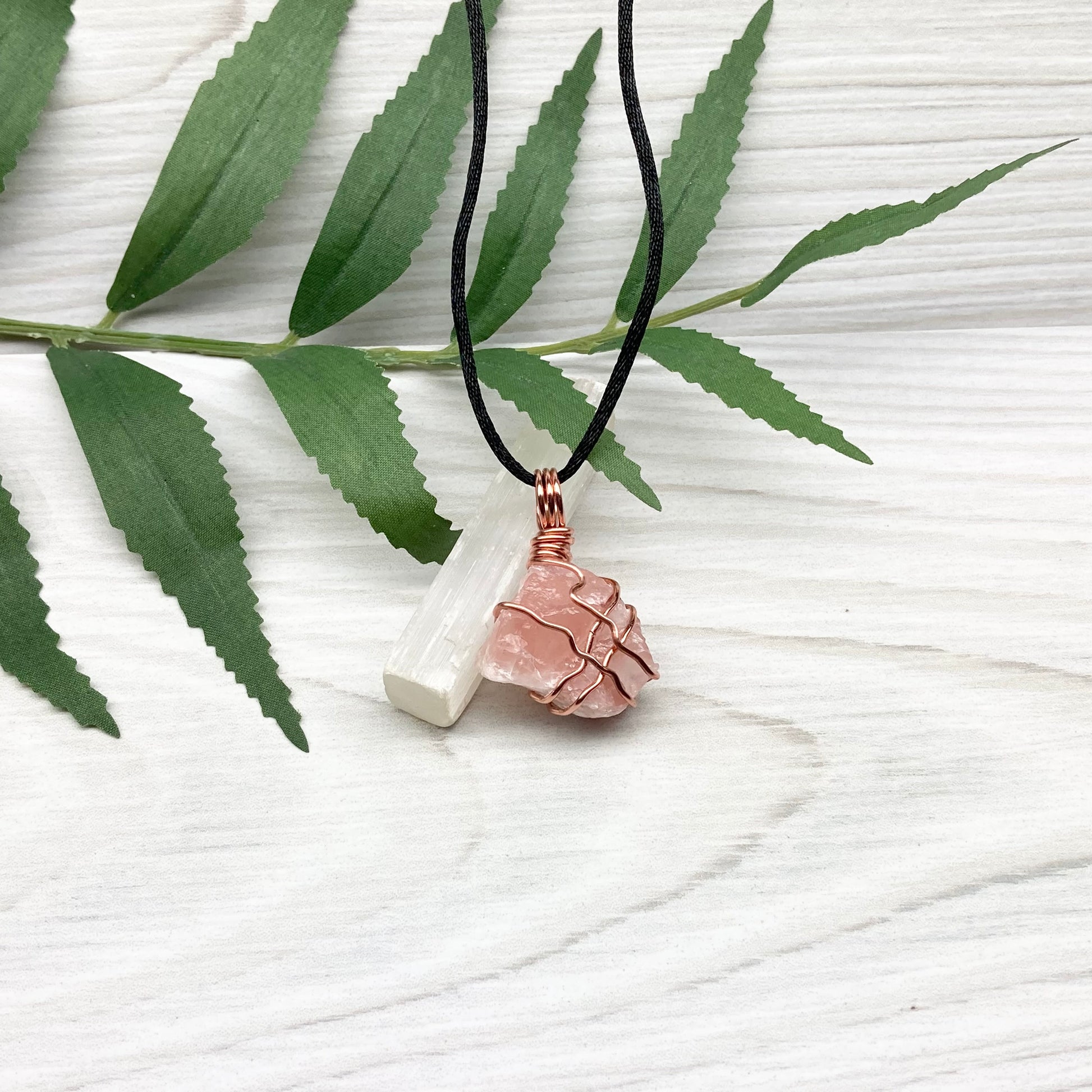 Necklace with a pink calcite stone pendant on a white background with green leaves.