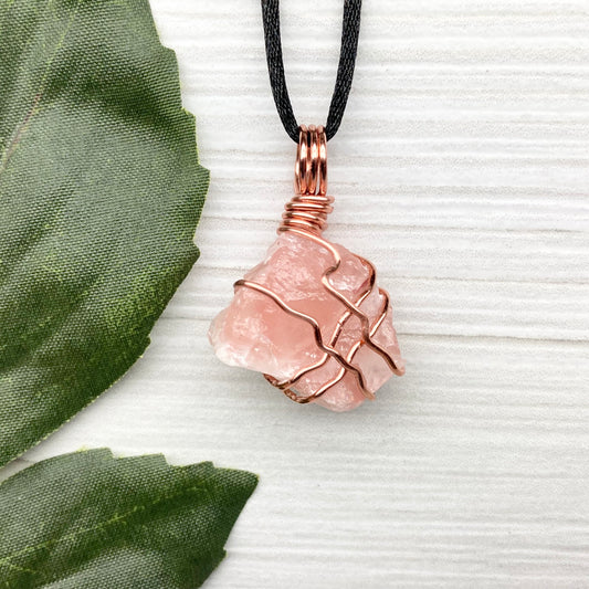 Necklace with a pink calcite stone pendant on a white background with green leaves.