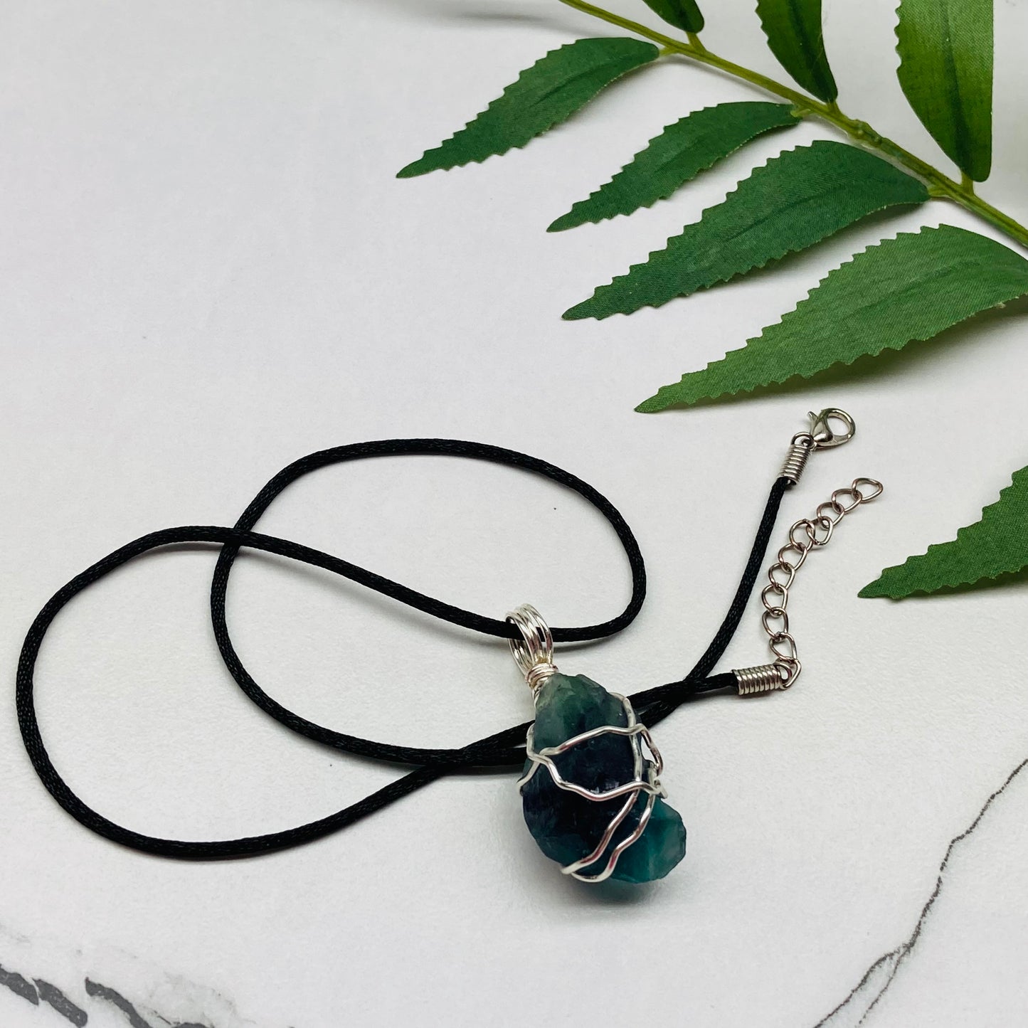 Rainbow Moonstone necklace. Raw blue and green stone wrapped with silver copper wire. Hangs on black chain.