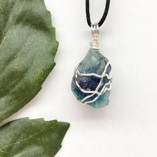 Rainbow Moonstone necklace. Raw blue and green stone wrapped with silver copper wire. Hangs on black chain. 