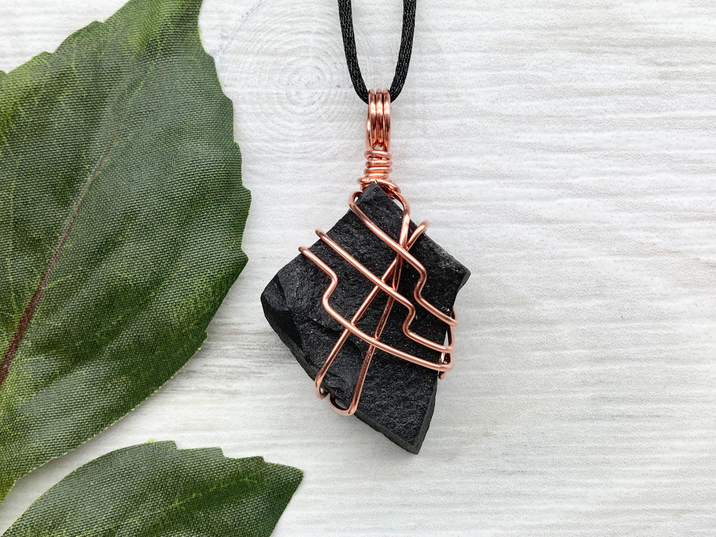 Black Agate stone wrapped with copper wire. Comes on a black satin silk necklace.