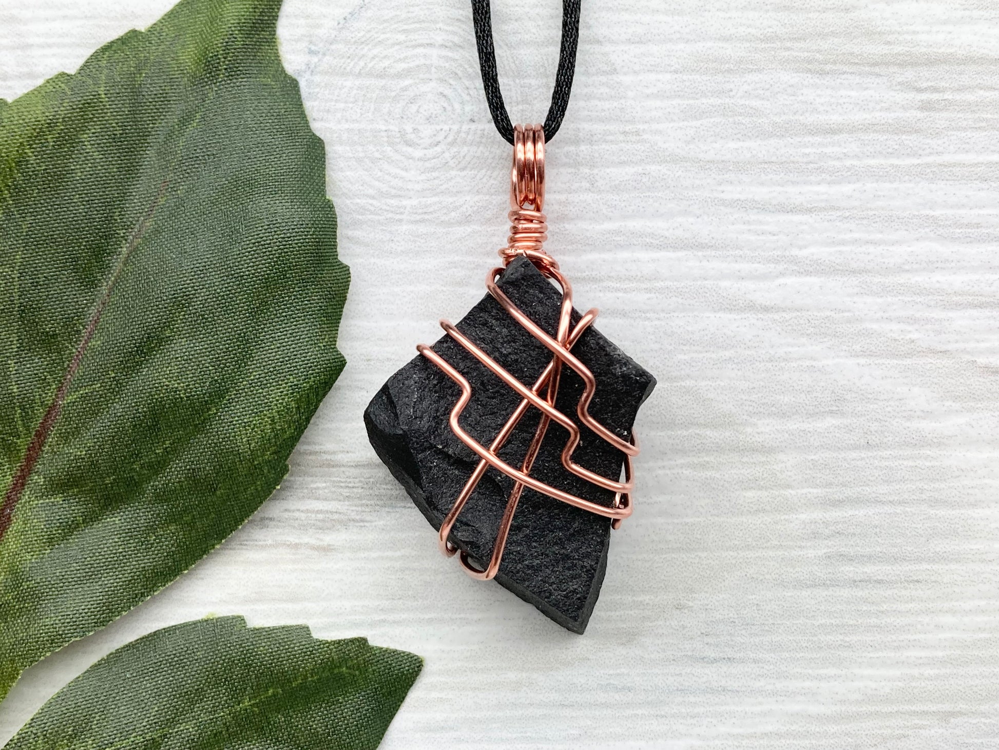 Black Agate stone wrapped with copper wire. Comes on a black satin silk necklace.