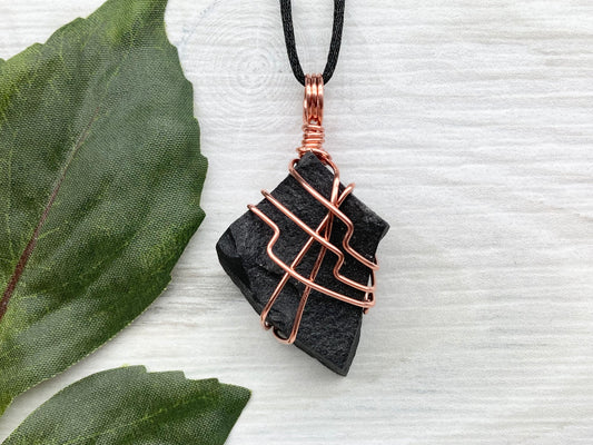 Black Agate stone wrapped with copper wire. Comes on a black satin silk necklace.