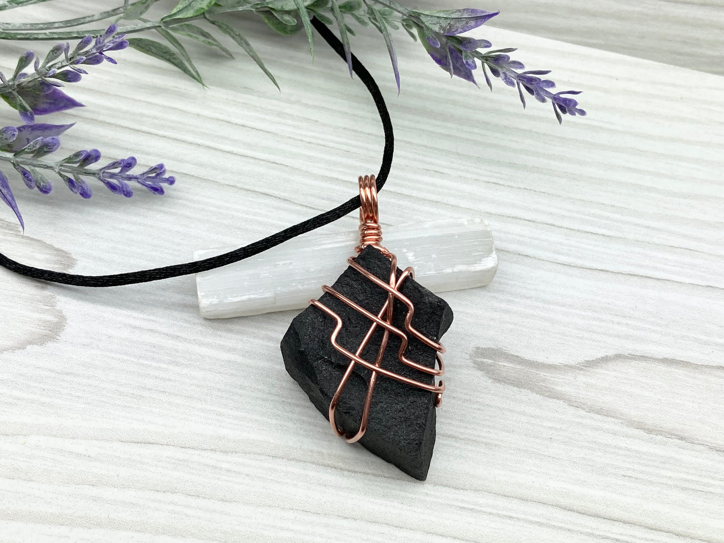 Black Agate stone wrapped with copper wire. Comes on a black satin silk necklace.