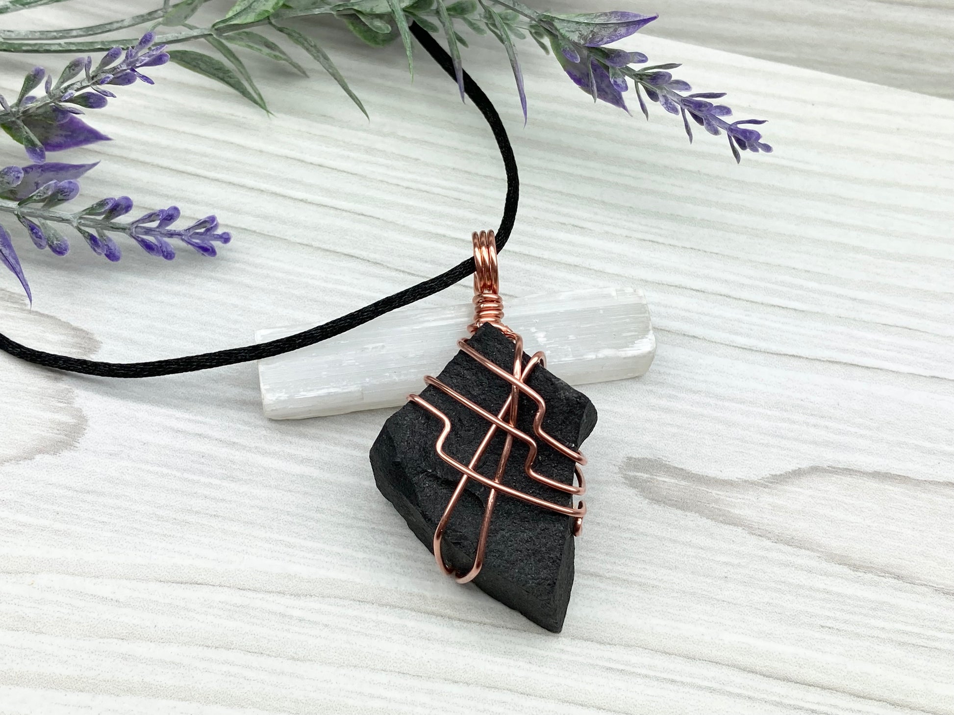 Black Agate stone wrapped with copper wire. Comes on a black satin silk necklace.