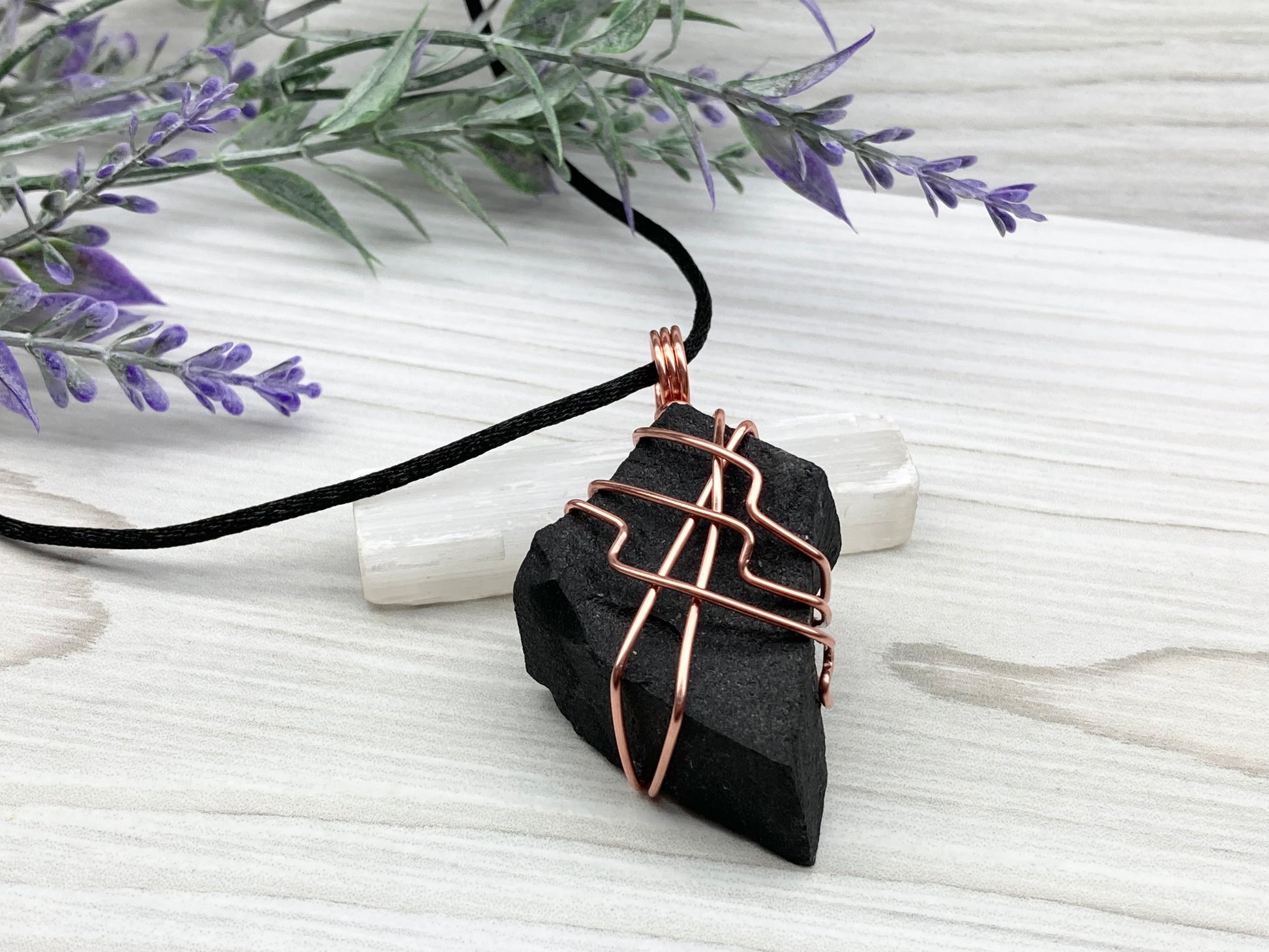 Black Agate stone wrapped with copper wire. Comes on a black satin silk necklace.