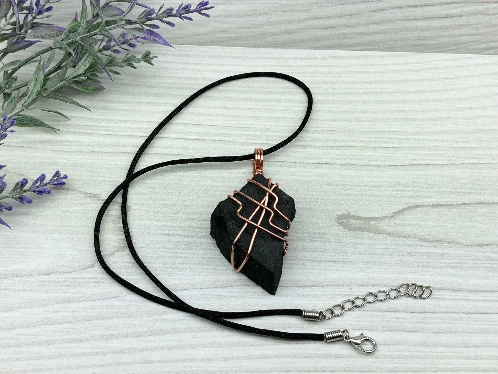 Black Agate stone wrapped with copper wire. Comes on a black satin silk necklace.