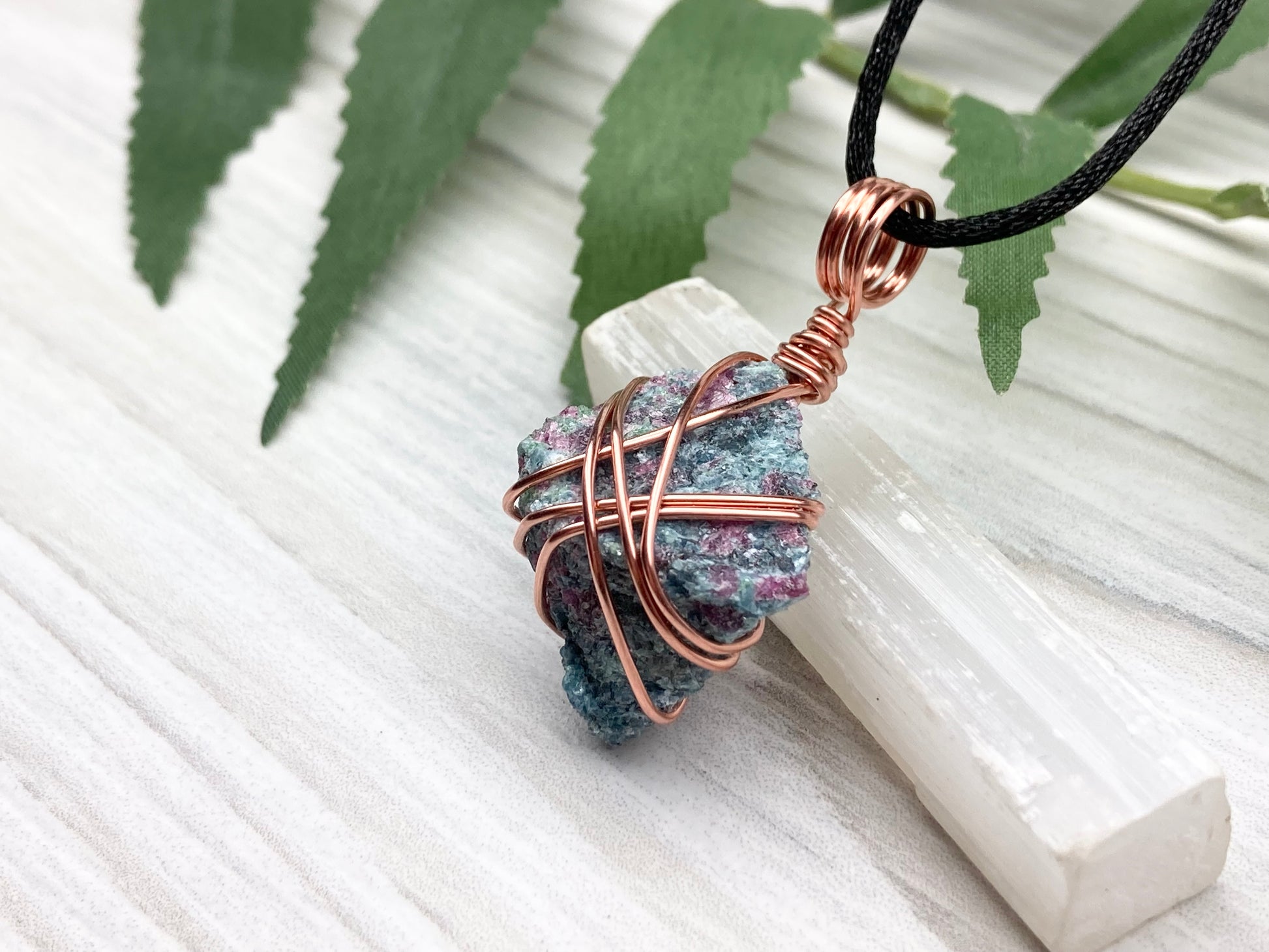 Rough Raw Ruby Zoisite Necklace. Left Side View. This Ruby Zoisite Crystal Is Hand Wrapped With Pure Copper Wire. This Stone is Blue and Red Colored. Gemstone Comes On A Black Chain. Spiritual New Age Style Unisex Jewelry.